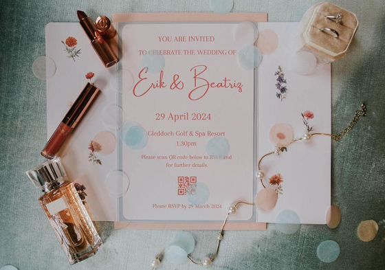 Pink and blue invitation with lipstick, perfume, wedding rings and jewellery